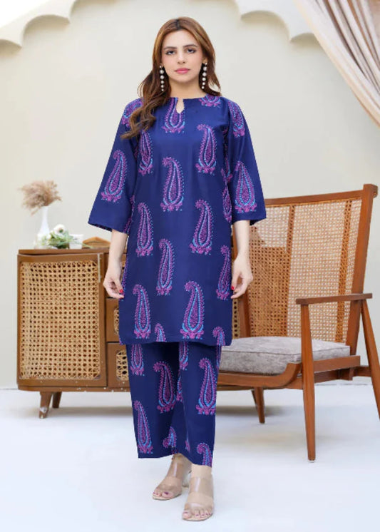 Woman wearing a blue patterned outfit standing in a room with a wooden chair and decorative arches.