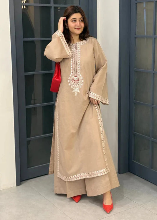 Woman in a beige embroidered outfit with red shoes and bag standing in front of gray doors.
